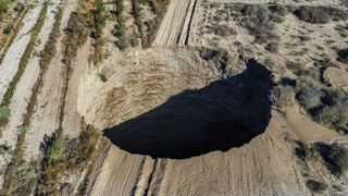 A huge deep circular sinkhole on an arid field with a path either side